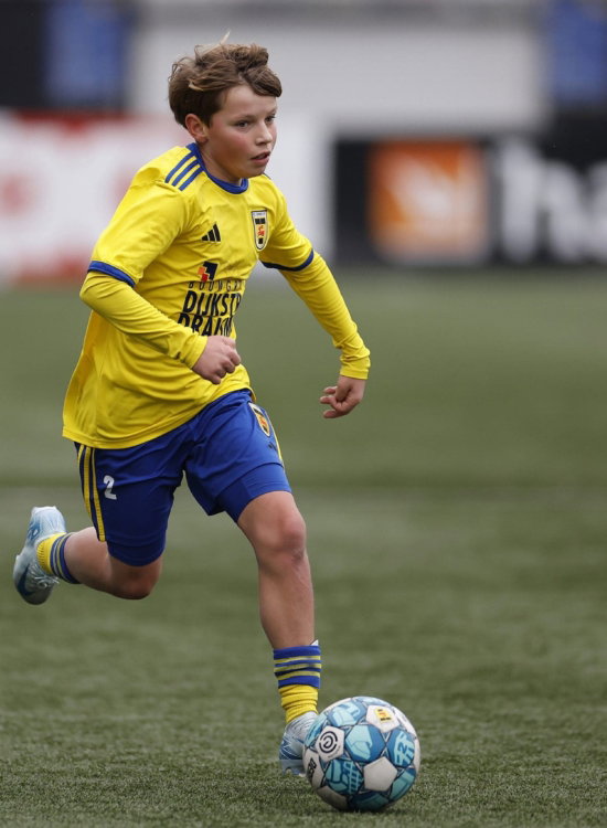 Jeugdspeler in geel dribbelt met de bal