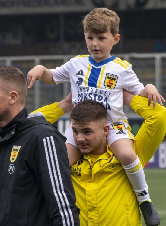 Speler met kind op de schouders langs het veld