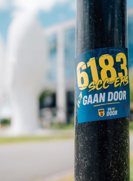 Sticker 6183 SCC'ers gaan door op een paal in de stad