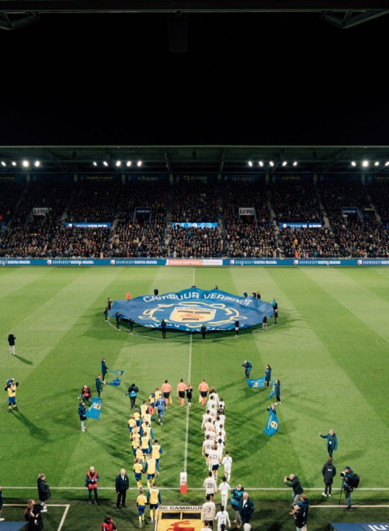 Opkomst van de spelers met spandoek op het veld