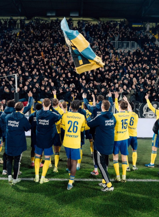 Spelers vieren met de supporters achter het doel