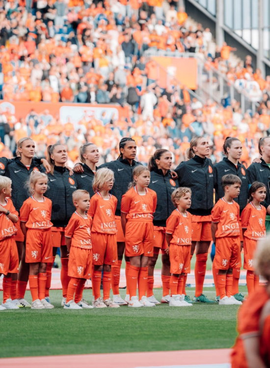 Meidenteams in oranje opgesteld in het stadion