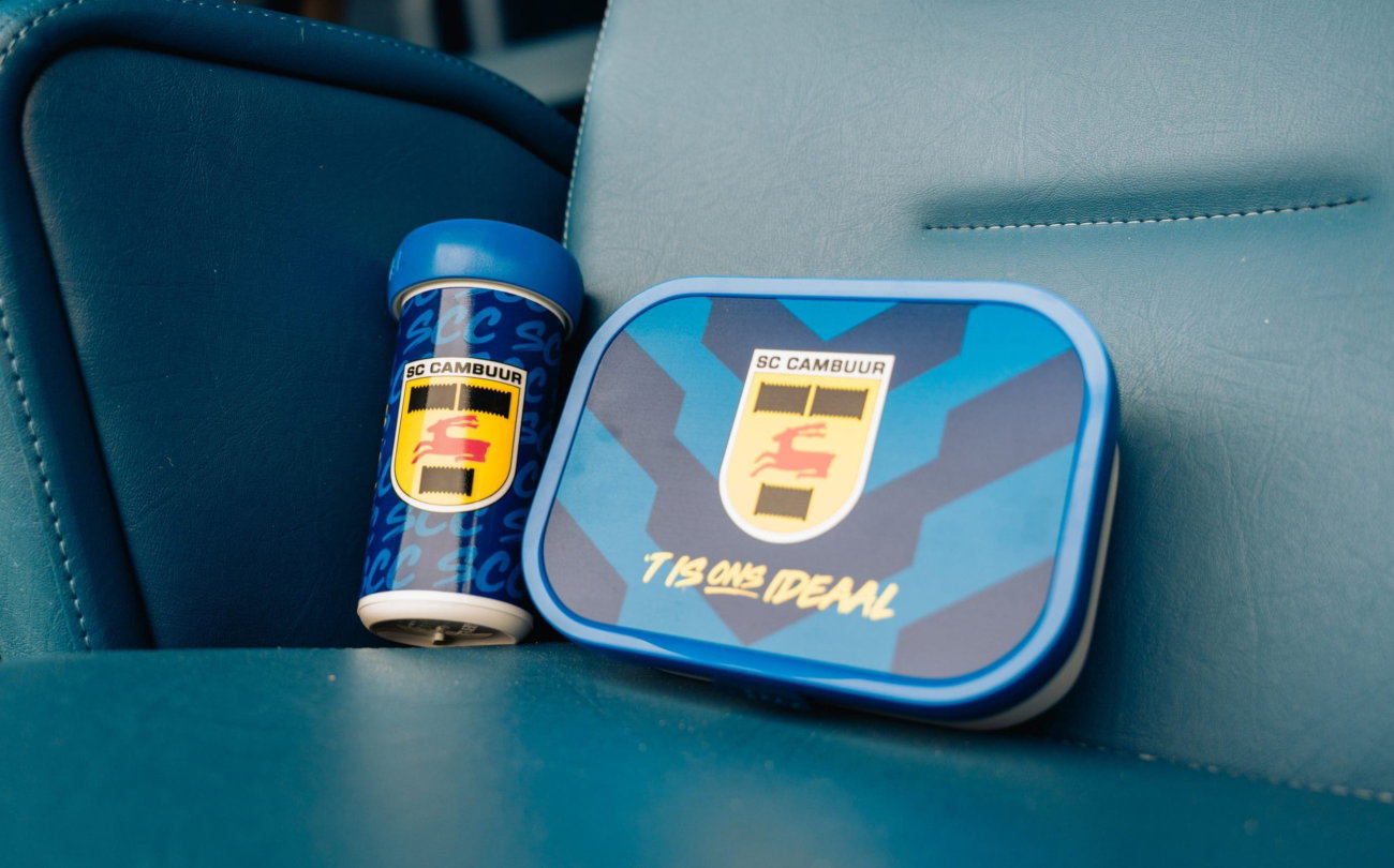 Cambuur-drinkbeker en broodtrommel op een stadionstoel