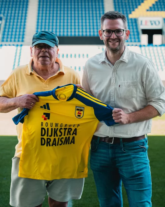 Partners met geel shirt op de tribune